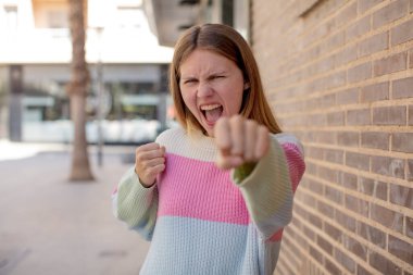 Güzel genç bir kadın kendinden emin, sinirli, güçlü ve agresif görünüyor. Yumrukları boks pozisyonunda dövüşmeye hazır.