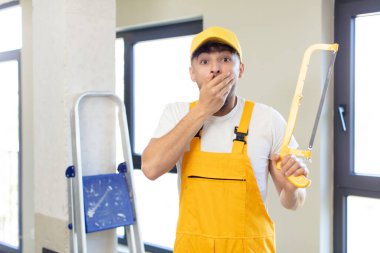 Genç ve yakışıklı bir adam ağzını eliyle kapatıyor ve şok olmuş ya da şaşırmış bir ifade takınıyor. Testereli tamirci.