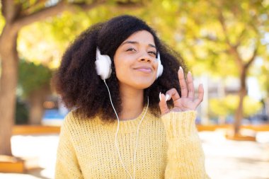 Güzel, afro siyah bir kadın kendini mutlu hissediyor. Onayını iyi bir jestle gösteriyor. kulaklıkla müzik dinlemek