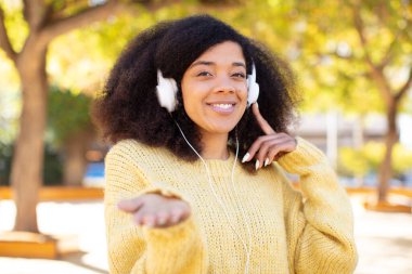Güzel afro siyah kadın mutlu bir şekilde gülümsüyor ve bir konsept sunuyor ya da gösteriyor. kulaklıkla müzik dinlemek