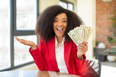 Oldukça afro siyah bir kadın inanılmaz bir şey karşısında mutlu ve şaşkın hissediyor. Dolar banknotları konsepti