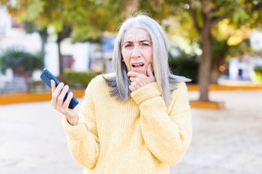 Ağzı ve gözleri sonuna kadar açık ve eli akıllı bir telefonla çenesinde olan son sınıf güzeli bir kadın.