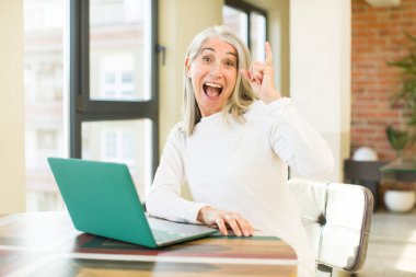 Dizüstü bilgisayarla bir fikri fark ettikten sonra mutlu ve heyecanlı bir dahi gibi hisseden son sınıf güzeli kadın.