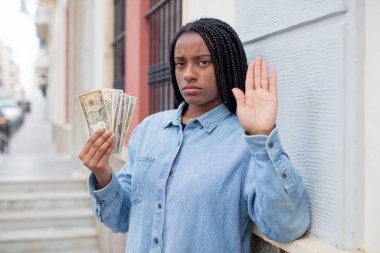 Siyah afro kadın ciddi görünüyor. Avuç içini gösteriyor. Durdurma hareketi yapıyor. Dolar banknotları konsepti