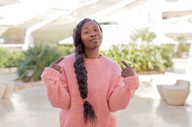 Afro güzel siyah kadın kötü tavırlı gururlu ve agresif görünüyor, yukarıyı gösteriyor ya da elleriyle alay işareti yapıyor.