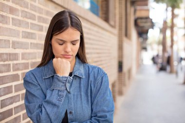 Genç ve güzel bir kadın ciddi, düşünceli ve endişeli, elleri çenesine bastırılmış bir şekilde yan bakıyor.