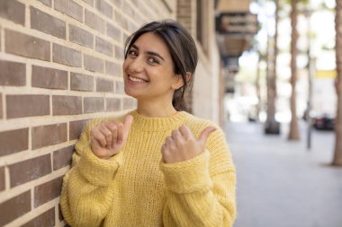 Güzel bir kadın neşeyle gülümsüyor ve yan taraftaki fotokopi alanını gösteriyor, mutlu ve tatmin olmuş hissediyor.