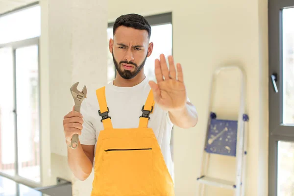 arab handsome man arab man looking serious showing open palm making stop gesture. handyman with a wrench