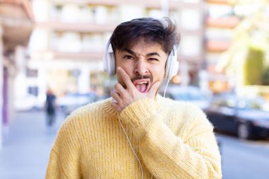 Ağzı ve gözleri açık ve eli çenesinde genç yakışıklı bir adam. kulaklıkla müzik dinlemek