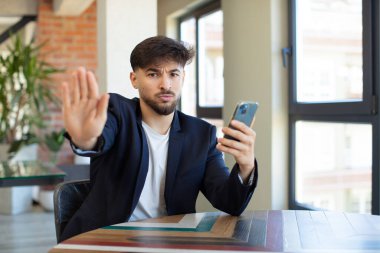 Genç ve yakışıklı adam ciddi görünüyor. Avuç içi gösteriyor. Durdurma hareketi yapıyor. akıllı telefon kavramı