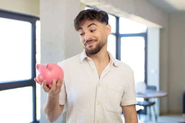 若いハンサムな男は 顎を手で幸せ 自信を持って表情で笑っている 貯金箱のコンセプト — ストック写真