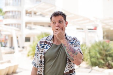 Yakışıklı bir adam elleri ile ağzını kapatıyor, şok olmuş, şaşırmış bir ifadeyle, sır saklıyor ya da 