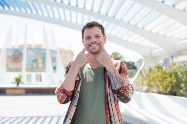 Yakışıklı adam kendine güvenerek sahte gülüşünü işaret ediyor.