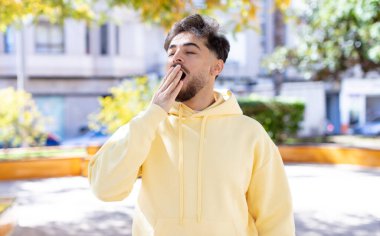 Genç yakışıklı adam tembelce esniyor, uykulu, yorgun ve sıkkın görünüyor.