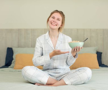 Genç, güzel bir kadın neşeyle gülümsüyor, mutlu hissediyor ve bir konsept gösteriyor. Kahvaltı kasesi konsepti