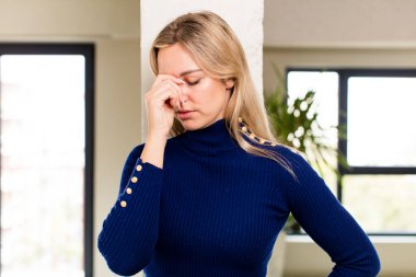 Genç ve güzel bir kadın stresli, mutsuz ve hayal kırıklığına uğramış, alnına dokunuyor ve şiddetli baş ağrısı çekiyor.