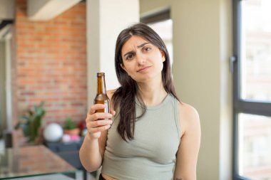 Genç bir kadın üzgün ve mızmızlanıyor. Mutsuz bir bakışı var ve ağlıyor. bira şişesi