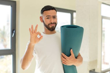 Arap yakışıklı adam mutlu hissediyor, iyi bir jestle onaylıyor. yoga mat konsepti
