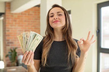 pretty woman feeling happy, showing approval with okay gesture. dollar banknotes concept