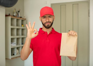 Genç yetişkin bir adam kendini mutlu hissediyor. Onayını iyi bir jestle gösteriyor. teslimatçı konsepti