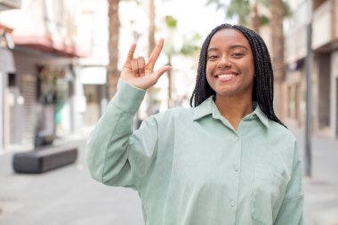 Afro güzel siyah kadın kendini mutlu, eğlenceli, kendinden emin, pozitif ve asi hissediyor, elle kaya ya da heavy metal işareti yapıyor.