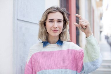 Güzel bir kadın elinde bir nesne tutuyor, küçük bir şeyi gösteriyor, sunuyor ya da reklamını yapıyor.