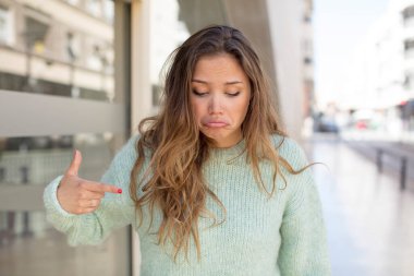 Güzel İspanyol kadın neşeyle gülümsüyor, yere bakıyor ve göğsüne işaret ediyor.