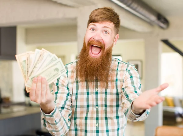 红头发的男人开心地笑着 用美元钞票提供或展示一个概念 — 图库照片