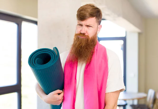 红头发的男人愁眉苦脸 哭哭啼啼 还带着瑜伽垫 健身概念 — 图库照片
