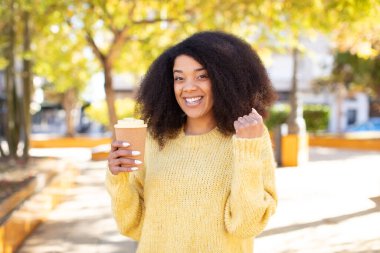 Oldukça afro siyah bir kadın şokta, gülüyor ve başarıyı kutluyor. kahve konseptini kaldır.