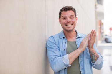 Yakışıklı adam kendini mutlu ve başarılı hissediyor, gülümsüyor ve alkışlıyor, alkışlarla tebrik ediyor.