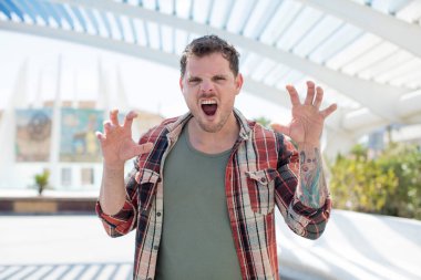 Yakışıklı adam panik ya da öfke içinde bağırıyor. Şok olmuş, korkmuş ya da öfkeli. Elleri başının yanında.