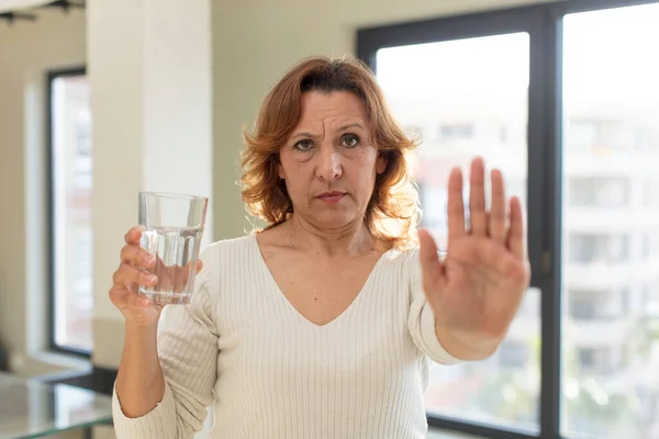 stock image middle age pretty woman looking serious showing open palm making stop gesture. water glass