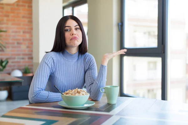 pretty young woman shrugging, feeling confused and uncertain. breakfast concept