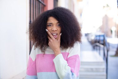 Afro-Amerikan güzel bir kadın ağzı ve gözleri açık ve eli çenesinde, nahoş bir şekilde şokta, ne ya da vay canına diyor.