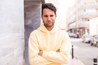 young hispanic man feeling displeased and disappointed, looking serious, annoyed and angry with crossed arms