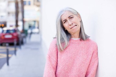 Yaşlı, emekli, güzel, beyaz saçlı, üzgün ve mızmız bir kadın. Mutsuz bir bakışla ağlıyor, olumsuz ve hayal kırıklığına uğramış bir tavırla.
