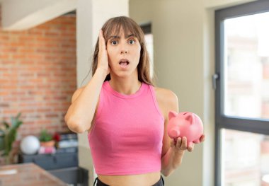 Genç ve güzel bir kadın son derece şaşırmış ve şaşırmış bir şekilde domuz kumbarası konsepti