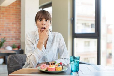 Ağzı ve gözleri açık, eli çenesinde genç ve güzel bir kadın. Ev yapımı kek konsepti