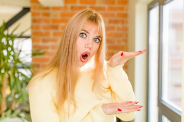 Genç ve güzel bir kadın şaşkın bir ifadeyle gülümsüyor ve elinde bir şey tutuyor. ev içi