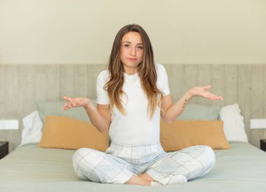 Güzel bir kadın omuz silkiyor, kafası karışık ve kararsız hissediyor. Gece elbisesi ve yatak odası konsepti