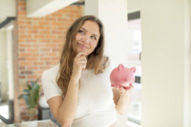 Güzel bir kadın mutlu, kendinden emin ve elleri çenesinde gülümsüyor. Domuz kumbarası konsepti