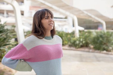 Güzel genç bir kadın endişeli, hasta, hasta ve mutsuz hissediyor. Ağrılı bir sırt ağrısı çekiyor.