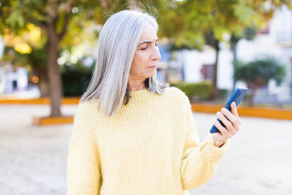 pretty senior woman smiling and looking with a happy confident expression with a smartphone