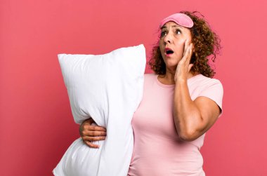 Güzel orta yaşlı kadın mutlu, heyecanlı ve şaşırmış pijama ve yastık giyiyor.