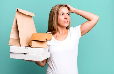 Güzel sarışın kadın şaşkın ve kafası karışık, kaşınıyor. Teslimat yiyecek paketleri kavramını kaldırır