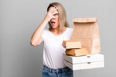 Güzel sarışın kadın şok olmuş, korkmuş ya da korkmuş görünüyor. Kağıt fast food paketleri götürür.