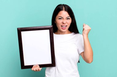 hispanic pretty woman shouting aggressively with an angry expression with an empty blank frame