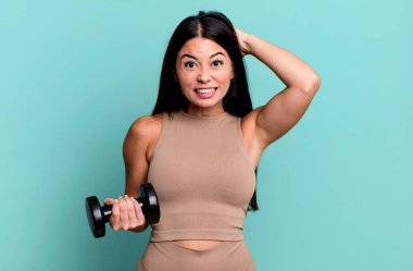 İspanyol güzel kadın kendini stresli, endişeli ya da korkmuş hissediyor, elleri başının üstünde. Fitness konsepti ve dambıl