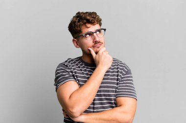 young adult caucasian man thinking, feeling doubtful and confused, with different options, wondering which decision to make